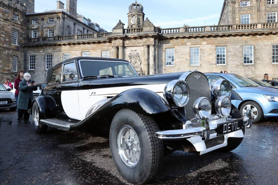 Custom Panther De Ville luxury car used in the Cruella film in a parking lot with a castle visible in the background.