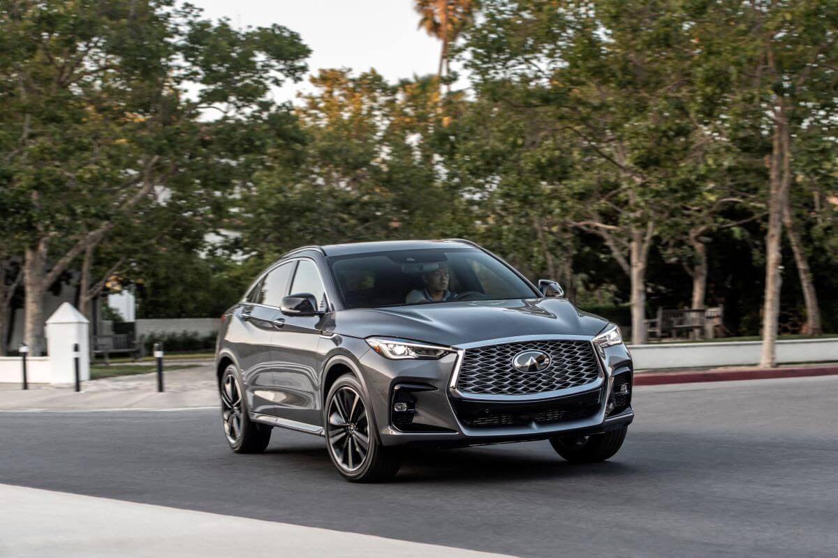 A dark-gray 2023 Infiniti QX55 luxury compact SUV model driving past a gate of bollards