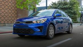 A blue 2023 Kia Rio subcompact sedan model driving through an urban city.