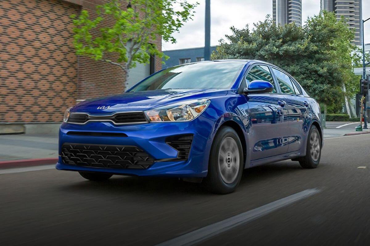 A blue 2023 Kia Rio subcompact sedan model driving through an urban city