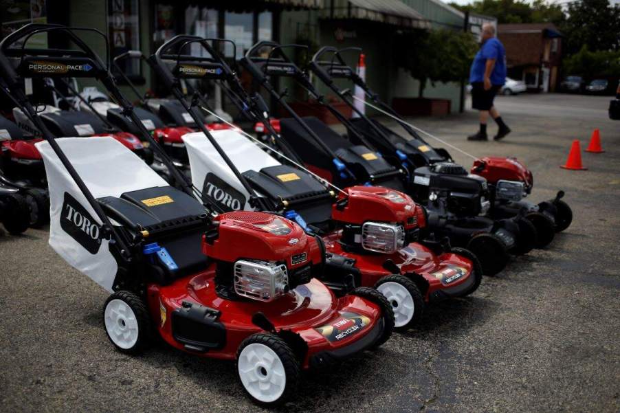 A row of lawn mowers, that may help with the consideration of electric vs. gas lawn mowers, all lined up outside of building.