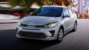 A silver-gray 2023 Kia Rio subcompact sedan model driving through an urban environment