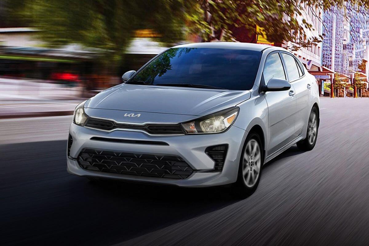 A silver-gray 2023 Kia Rio subcompact sedan model driving through an urban environment