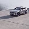 A silver-gray 2023 Volvo XC60 compact luxury SUV model parked on a concrete dock near the water.