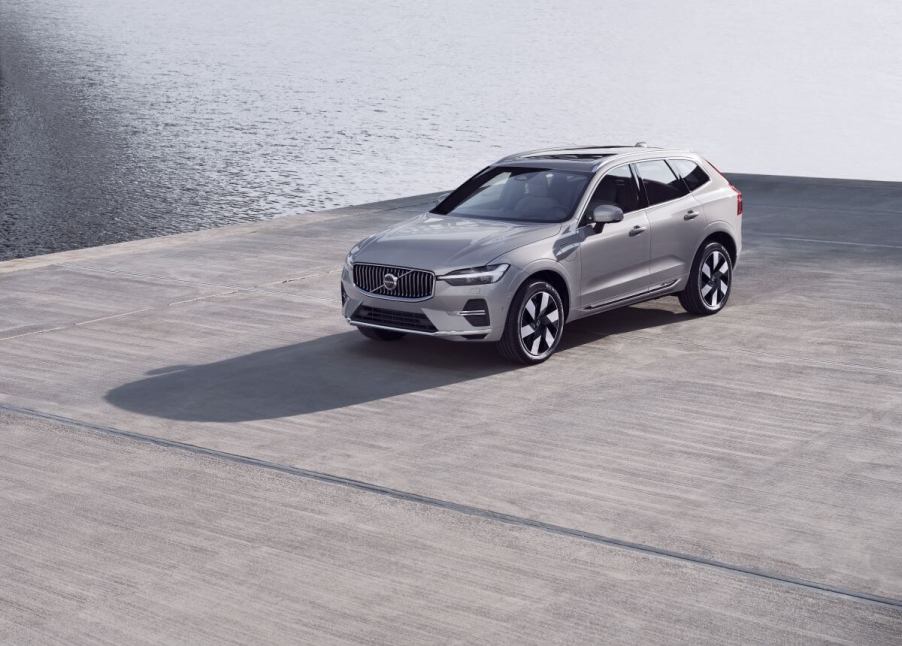 A silver-gray 2023 Volvo XC60 compact luxury SUV model parked on a concrete dock near the water.