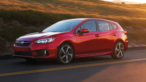 A red 2023 Subaru Impreza Hatchback model driving on a country highway as the sun sets behind it