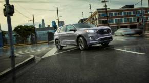 A 2023 Ford Edge midsize SUV model driving on wet city roads as it passes through a streetlight intersection