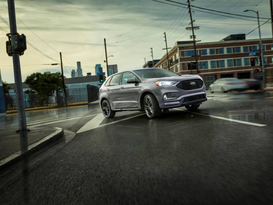 A 2023 Ford Edge midsize SUV model driving on wet city roads as it passes through a streetlight intersection