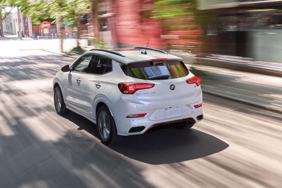 A rear shot of white 2023 Buick Encore GX subcompact SUV model driving through a city with a blurred background