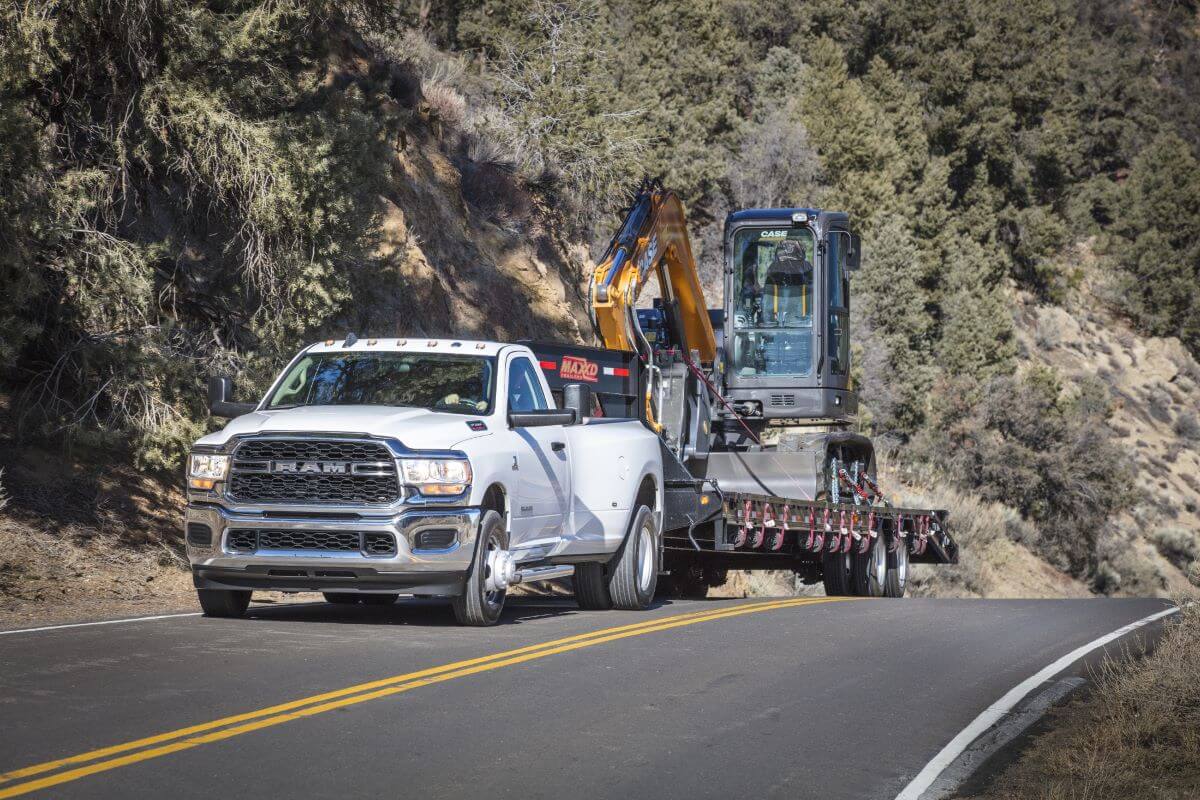 A white 2023 Ram 3500 HD heavy-duty pickup truck model towing a front loader construction excavation vehicle