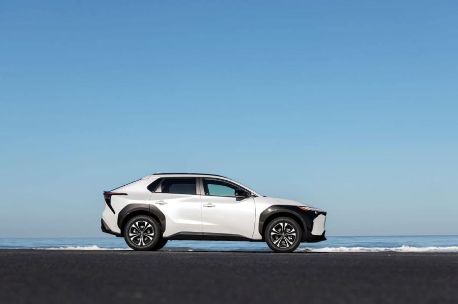 A side profile shot of a 2023 Toyota bZ4X compact electric SUV model in Wind Chill Pearl set against the sea