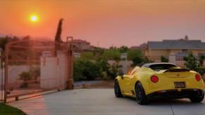 The Alfa Romeo 4C exotic Italian sports car parked in a driveway, the setting sun visible in the background.