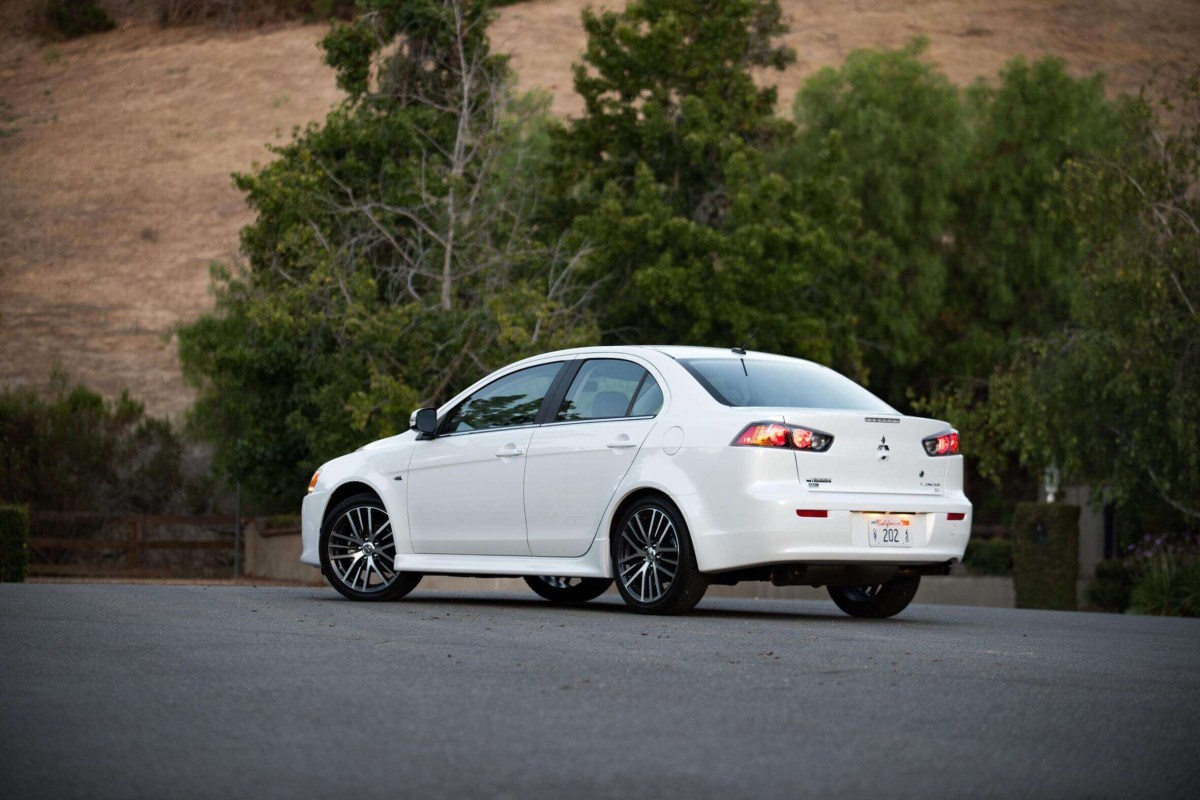 Out of all Mitsubishi models, maintenance is less of a concern for the Lancer among other sedans in the lineup, though it can still get expensive. This white sedan is on the road with trees in the background.