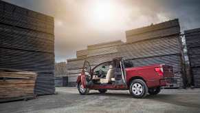 A red Nissan Titan parked in a lumber yard with its rear-hinged rear doors open.