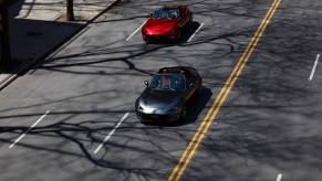 Two Mazda MX-5 Miata (one gray, the other black) models on a city street.