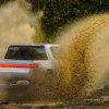 A Rivian R1T electric truck racing across a dirt road, dust visible in the foreground.