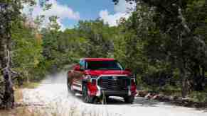 Red 2022 Toyota Tundra pickup truck driving down a dirt road, dust visible behind it.