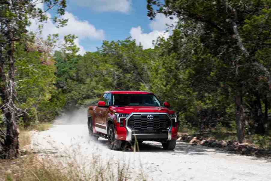 Red 2022 Toyota Tundra pickup truck driving down a dirt road, dust visible behind it.