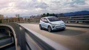 A light blue 2023 Chevy Bolt EV electric car cruises down a highway.