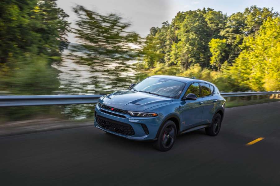 A blue 2023 Dodge Hornet GT drives quickly with green trees in the background.