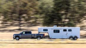 A Ford Super Duty with a 40,000 pound maximum towing capacity pulls a trailer down the road, trees a blur in the background.