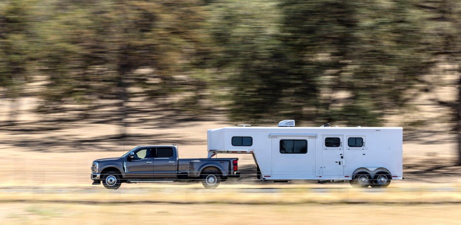 A Ford Super Duty with a 40,000 pound maximum towing capacity pulls a trailer down the road, trees a blur in the background.