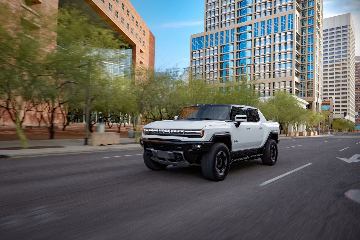 A white 2023 GMC Hummer EV Edition1 all-electric pickup truck model driving on a city road with Super Cruise