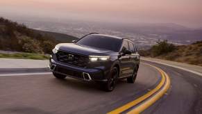 A black 2023 Honda CR-V Sport Touring SUV traveling uphill on a two-lane highway