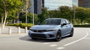 A gray-blue 2023 Honda Civic Si drives on urban streets.