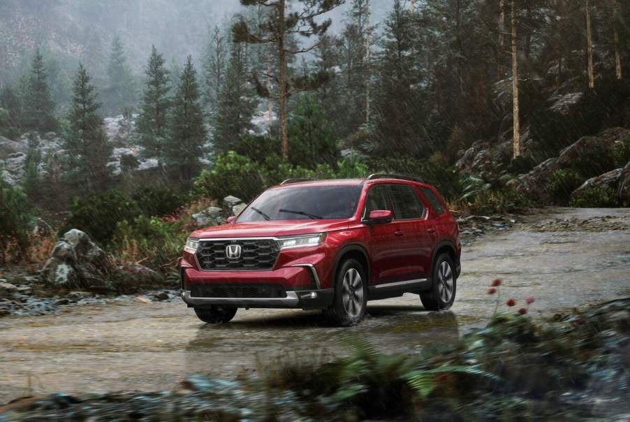 A red 2023 Honda Pilot Elite midsize SUV parked on a mountain road amid pine trees in the rain