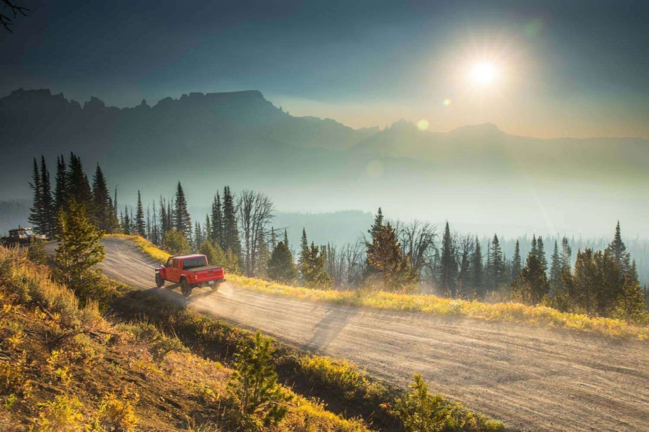 A Jeep Gladiator driving over a dirt trail on an American mountain top, a sunset visible in the background.