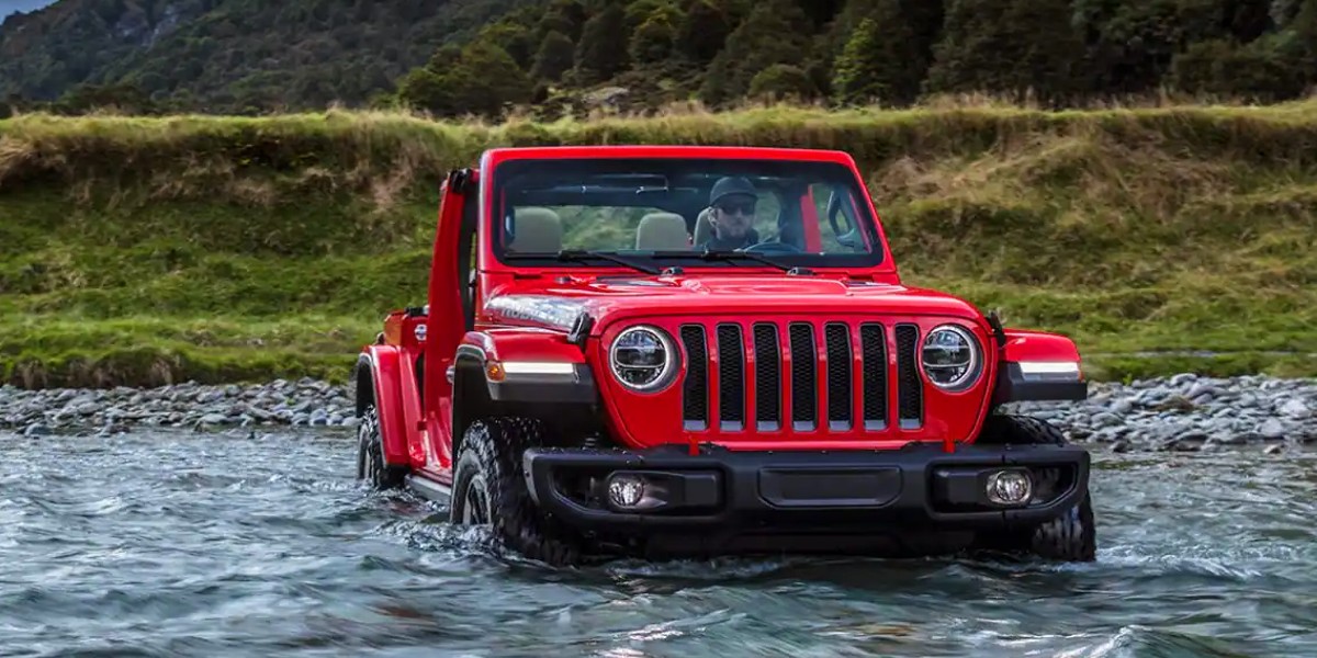 A red 2023 Jeep Wrangler small SUV is driving through water.