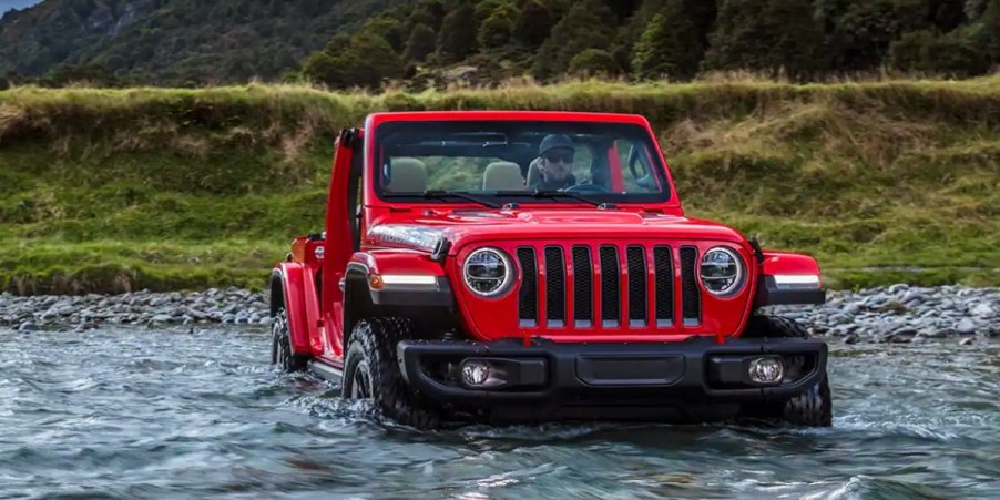 A red 2023 Jeep Wrangler small SUV is driving through water.