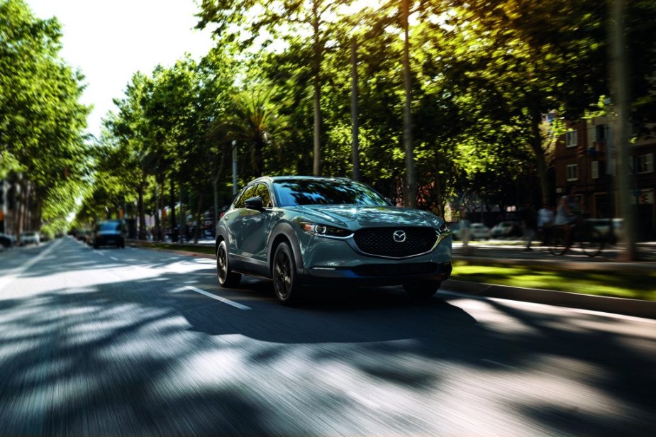 A Mazda CX-30 subcompact SUV drivers down a road with blurred trees on either side.