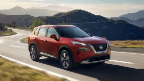 A red 2023 Nissan Rogue small SUV is driving on the road.