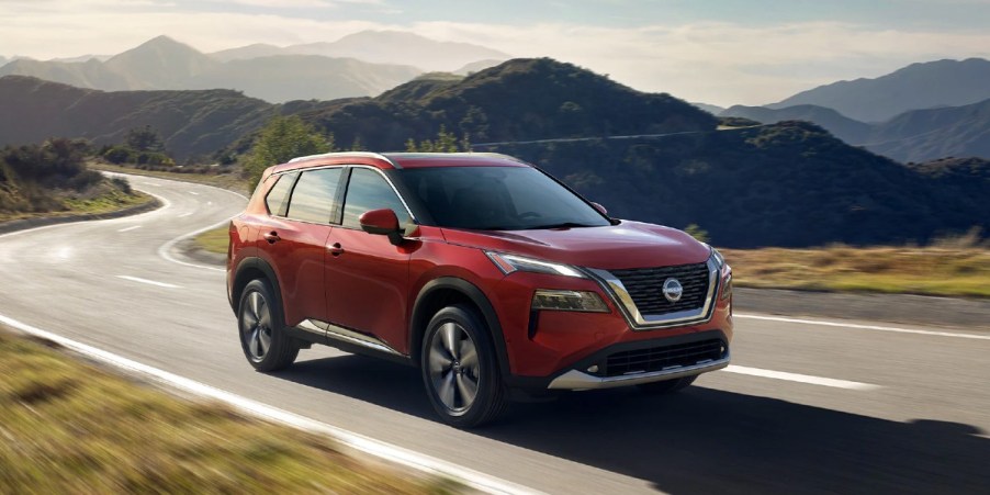 A red 2023 Nissan Rogue small SUV is driving on the road.