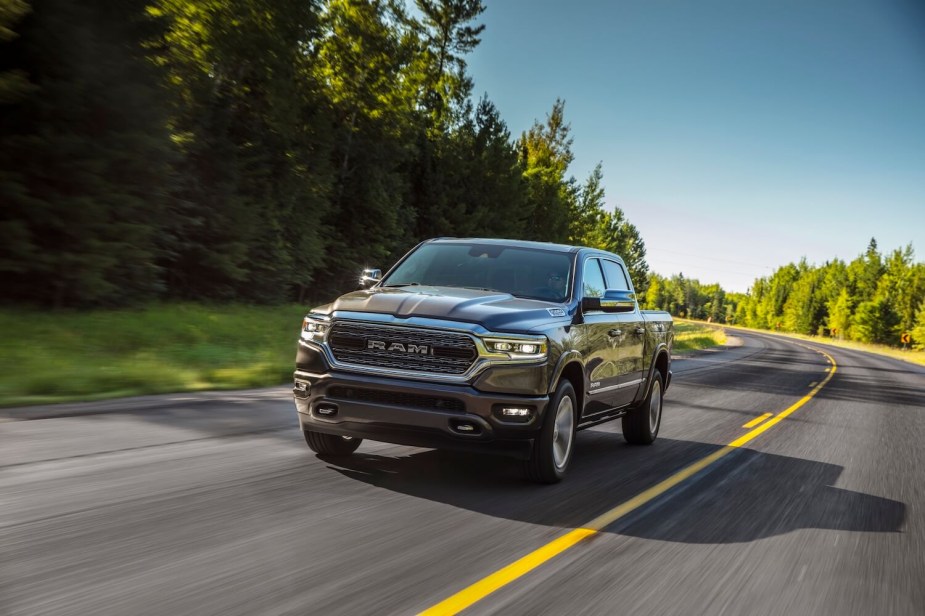 A Ram 1500 drives down an empty road, trees visible in the background.