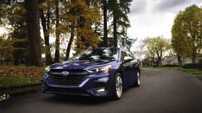 Blue 2023 Subaru Legacy driving down a suburban road.