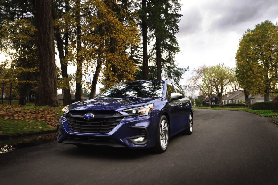 Blue 2023 Subaru Legacy driving down a suburban road.