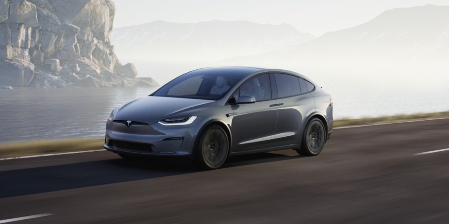 A gray 2023 Tesla Model X luxury electric midsize SUV is driving on the road. 