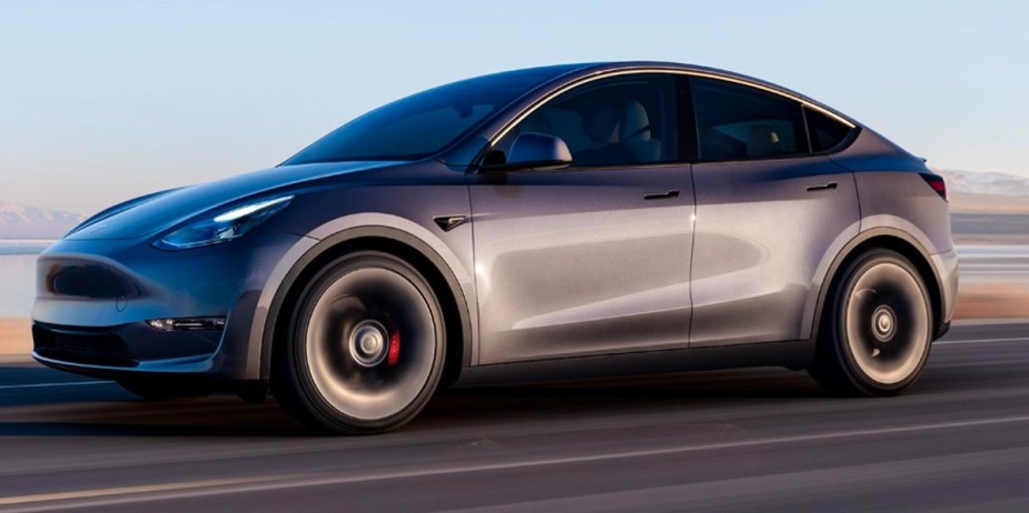 A gray 2023 Tesla Model Y small electric SUV is driving on the road. 