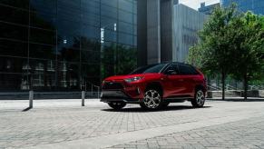 A red 2023 Toyota RAV4 Prime XSE plug-in hybrid electric vehicle (PHEV) model outside a glass office building