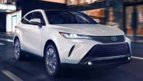 A white 2023 Toyota Venza midsize hybrid SUV is driving on the road.