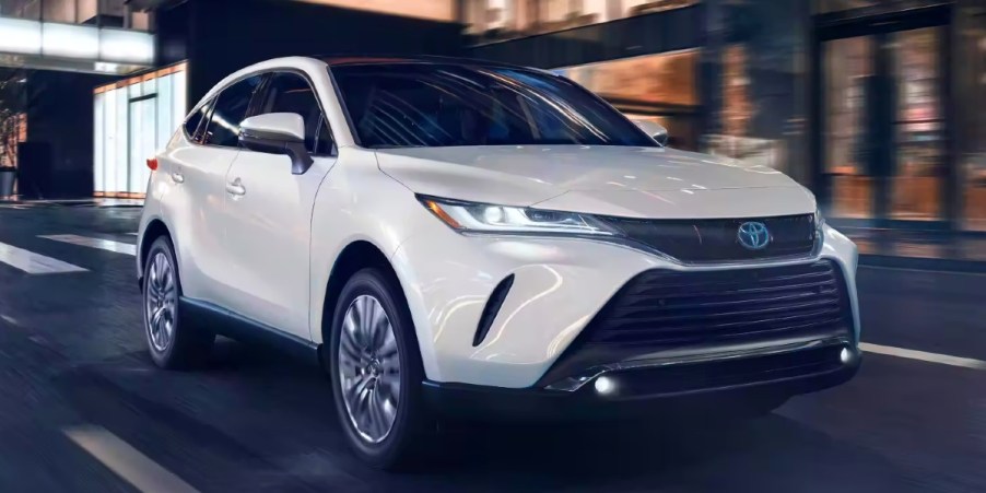 A white 2023 Toyota Venza midsize hybrid SUV is driving on the road.