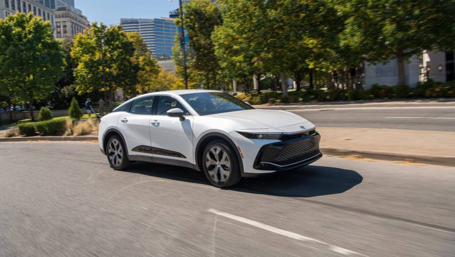 A white 2023 Toyota Crown, one of the competitors to the Tesla Model 3, driving down a city street.