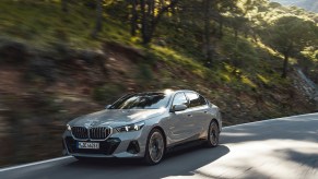 A Gray 2024 BMW 5 Series driving down a forest road