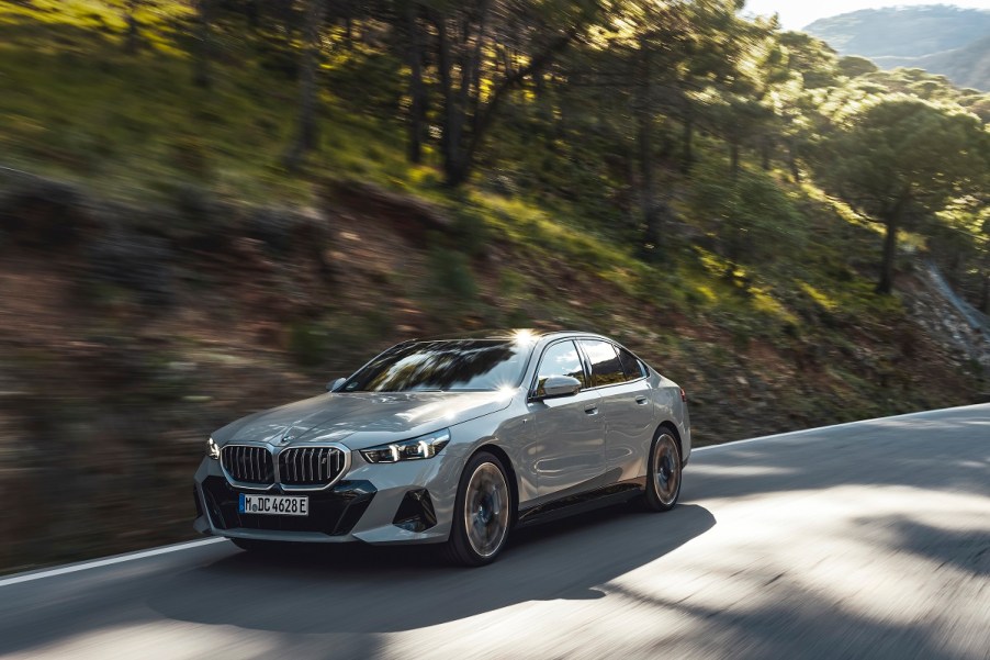 A Gray 2024 BMW 5 Series driving down a forest road