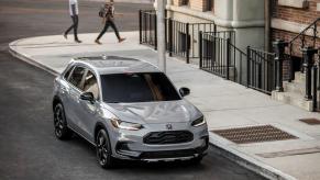 A gray 2024 Honda HR-V Sport subcompact SUV model parked on the side of a city street near a sewer grate