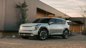 A 2024 Kia EV9 midsize electric SUV model parked on dirt outside of a gray shutter garage