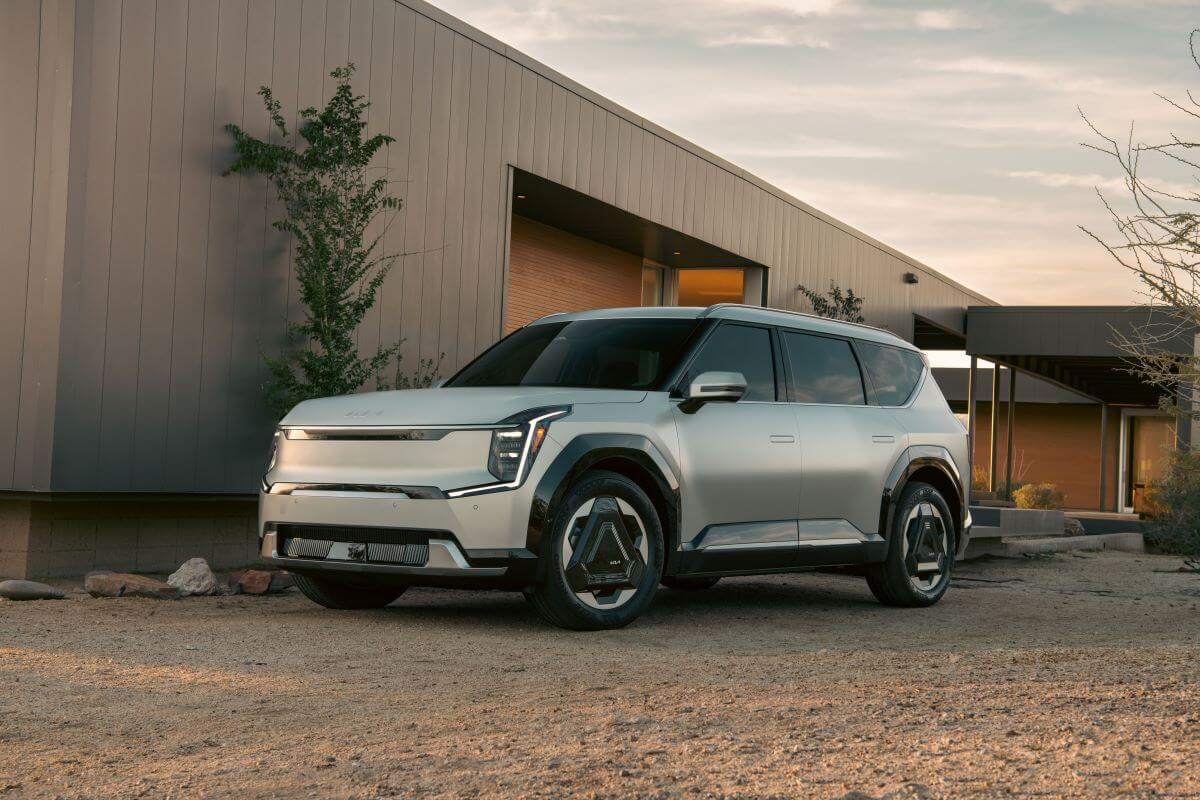 A 2024 Kia EV9 midsize electric SUV model parked on dirt outside of a gray shutter garage